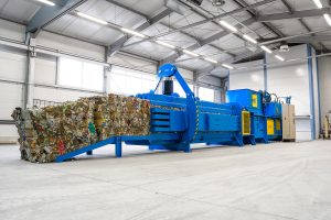Industrial channel baler with automated wire tying system compressing mixed recyclable materials into dense, uniform bales inside a modern waste-processing facility.