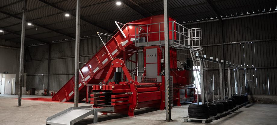 ANIS high-capacity cardboard baler bale density system with inclined feed conveyor and automatic tying line inside a recycling facility.