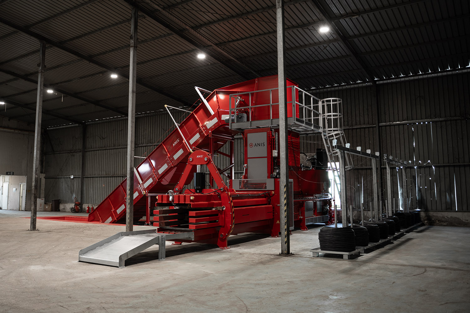 ANIS high-capacity cardboard baler bale density system with inclined feed conveyor and automatic tying line inside a recycling facility.