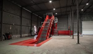 Industrial cardboard baler with in-ground conveyor system inside a recycling facility, designed for high-density bale production and efficient material handling.