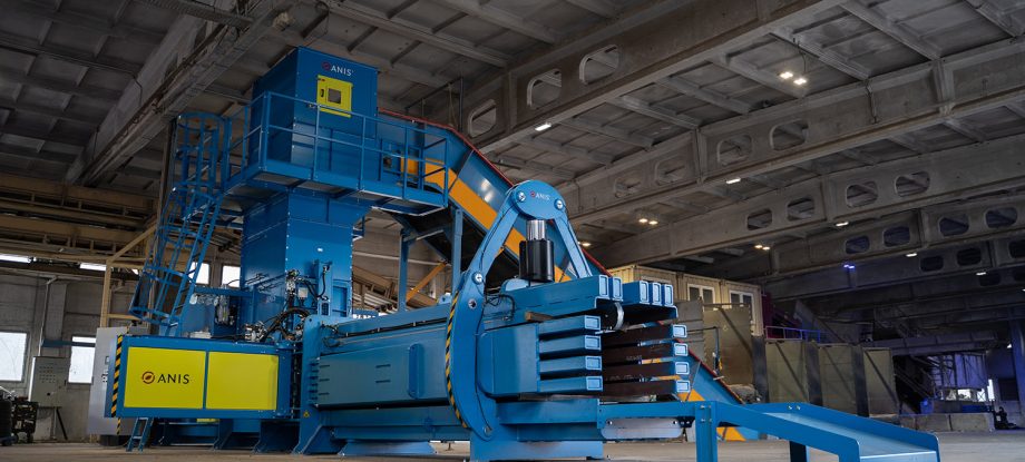 High-capacity industrial channel baler equipped with an automatic baler wire tying system operating inside a large recycling facility.