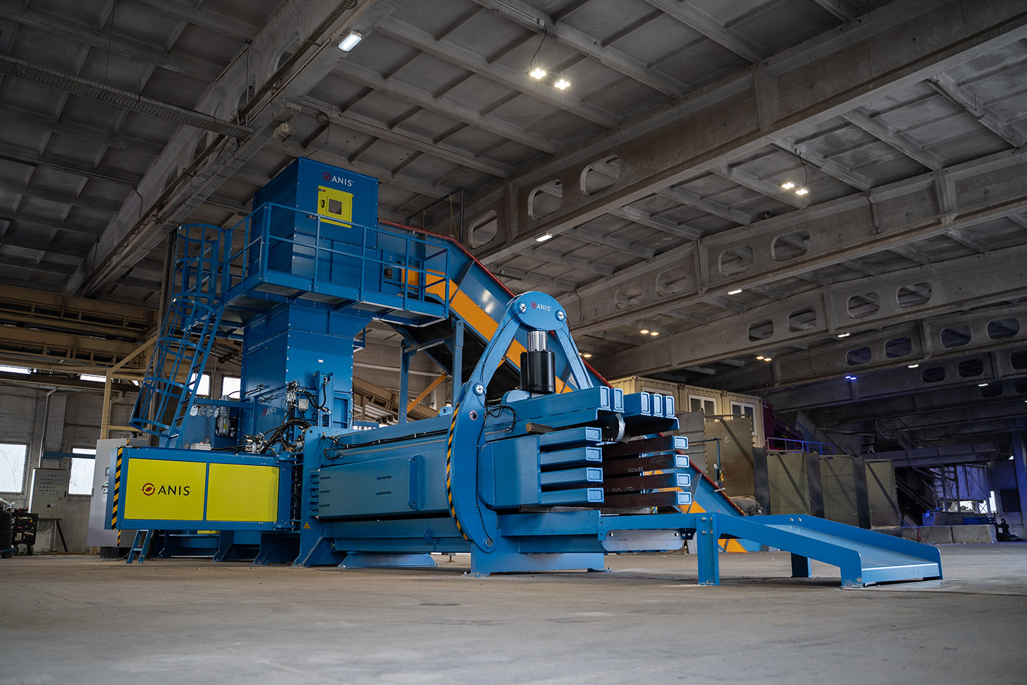 High-capacity industrial channel baler equipped with an automatic baler wire tying system operating inside a large recycling facility.