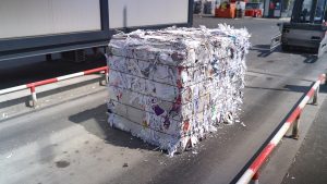 Compacted bale of shredded and mixed paper tightly secured with baler wire, ready for transport from a recycling facility.