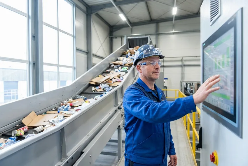 An operator monitoring a conveyor belt feeding materials into a channel baling press.