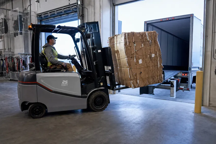 Elektrischer Gabelstapler verlädt einen hochverdichteten Kartonballen an der Laderampe eines Logistikzentrums.