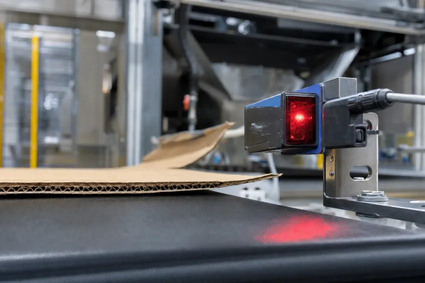 Makroaufnahme eines optischen Sensors an einem Förderband, der einen Karton für die Ballenpresse erkennt.