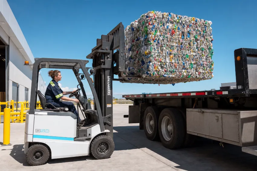 Eine Logistikmitarbeiterin verlädt mit einem Elektrostapler einen dichten Kunststoffballen auf einen LKW.